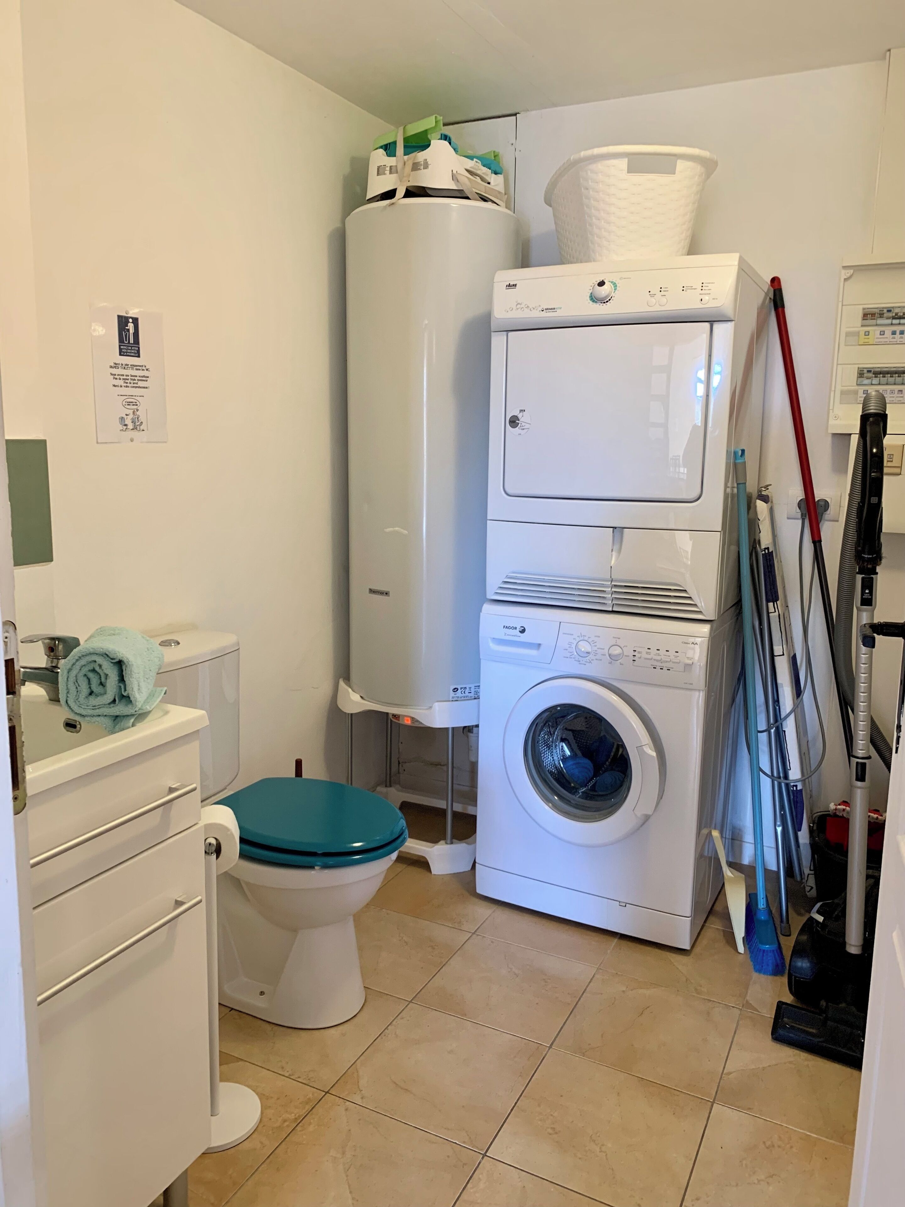 Une petite salle de bain comprenant des toilettes, un lave-linge et des paniers à linge empilés.
