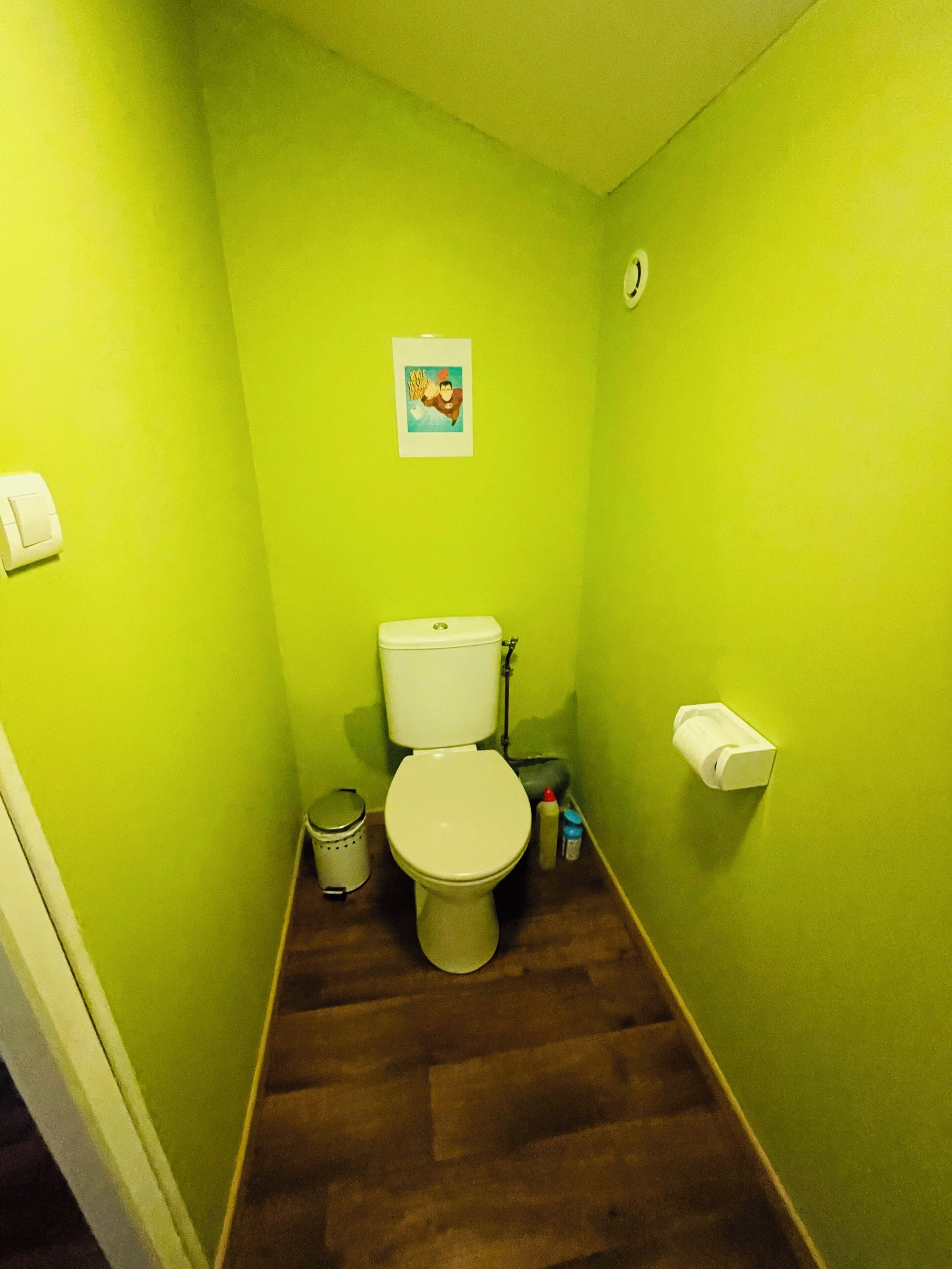 A small bathroom with a toilet, a trash can, and a toilet paper holder on the wall.