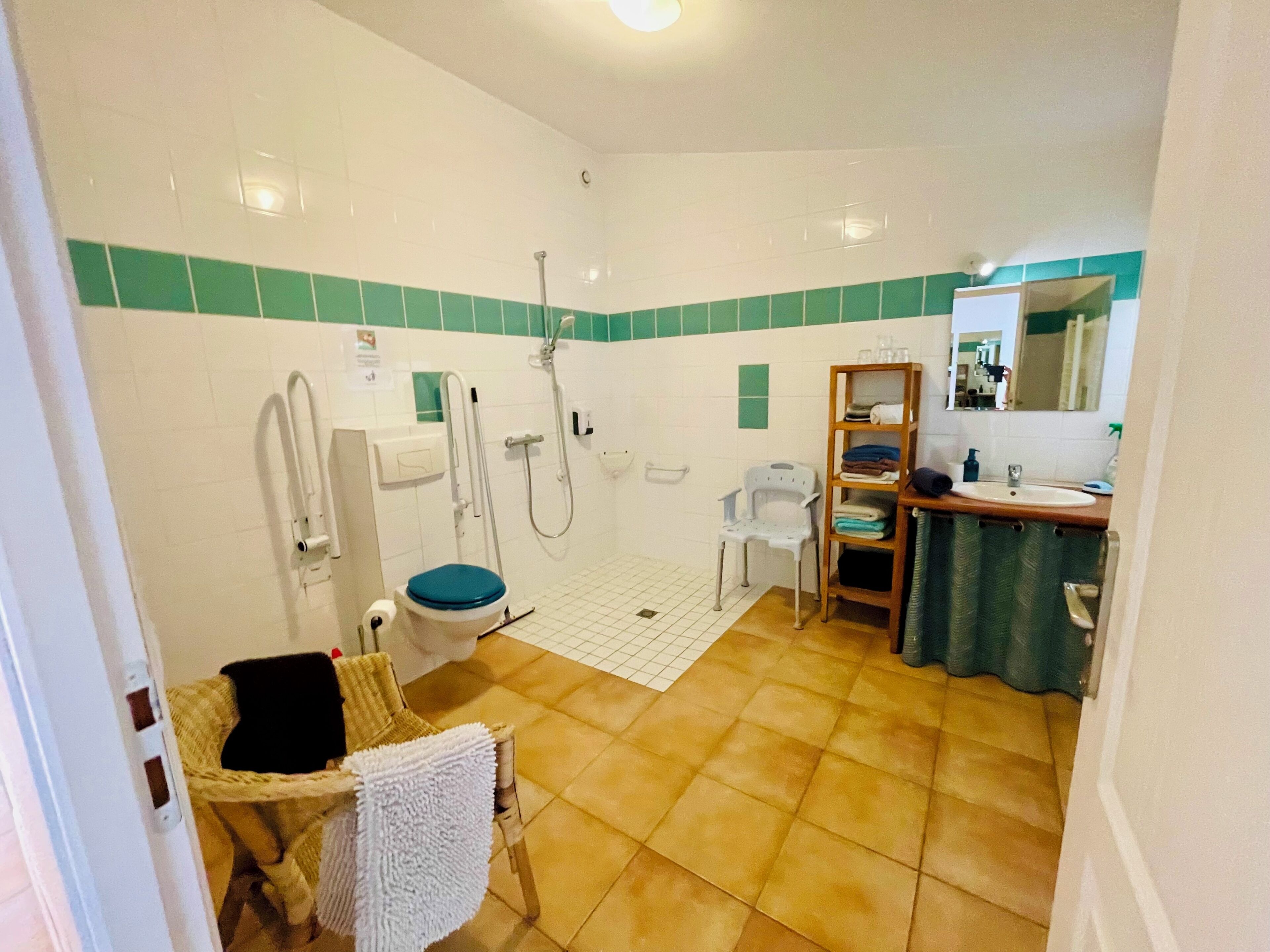 A bathroom with a shower, toilet, and sink, a chair with a towel, and a mirror.