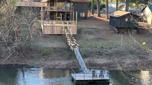 A cabin with a deck extending over a body of water, connected by a wooden walkway.