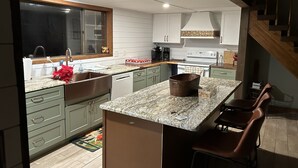 A modern kitchen with a central island, white cabinetry, and a wooden staircase.