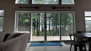 Een modern interieur met een grote schuifdeur naar een terras, een eethoek met tafel en stoelen, en een zithoek met kussens.