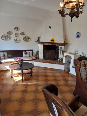 Cozy living room with a fireplace, comfortable sofa, and wooden chair, surrounded by decorative plates and a chandelier.