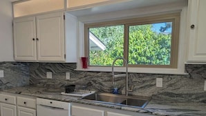A kitchen with white cabinets, a granite countertop, a stainless steel sink, and a window with a view of greenery. - Sparkling Clean, Private & Quiet! Amazing Ocean Views [3] (Brookings)