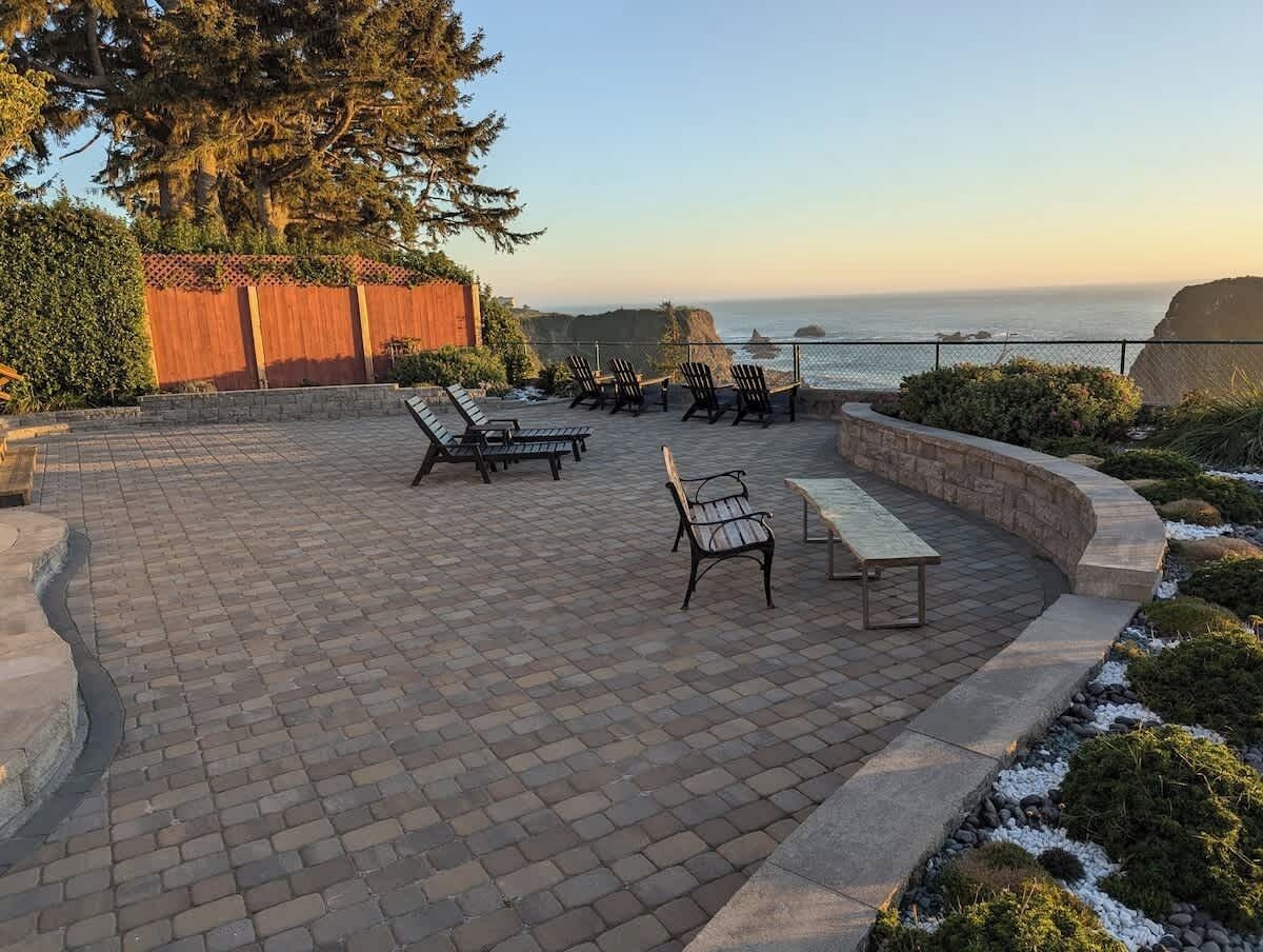 Eine Terrasse im Freien mit Backsteinböden, mehreren Holzbänken und Blick aufs Meer.
