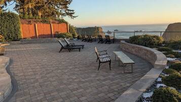 Eine Terrasse im Freien mit Backsteinböden, mehreren Holzbänken und Blick aufs Meer.
