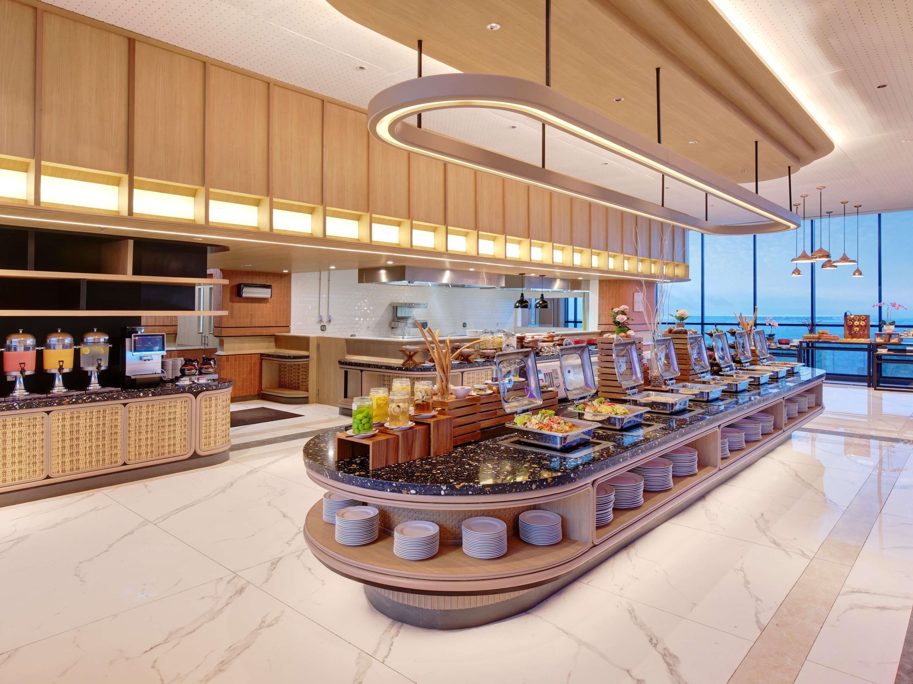 Disposição de buffet com diversas estações de comida, área de cozinha e vista para o mar.
