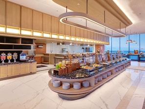 A buffet setup with various food stations, a kitchen area, and a view of the sea. - Novotel Yogyakarta International Airport Kulon Progo (Temon)
