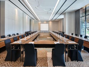 A conference room with a long table, chairs, a projector screen, and a carpeted floor.