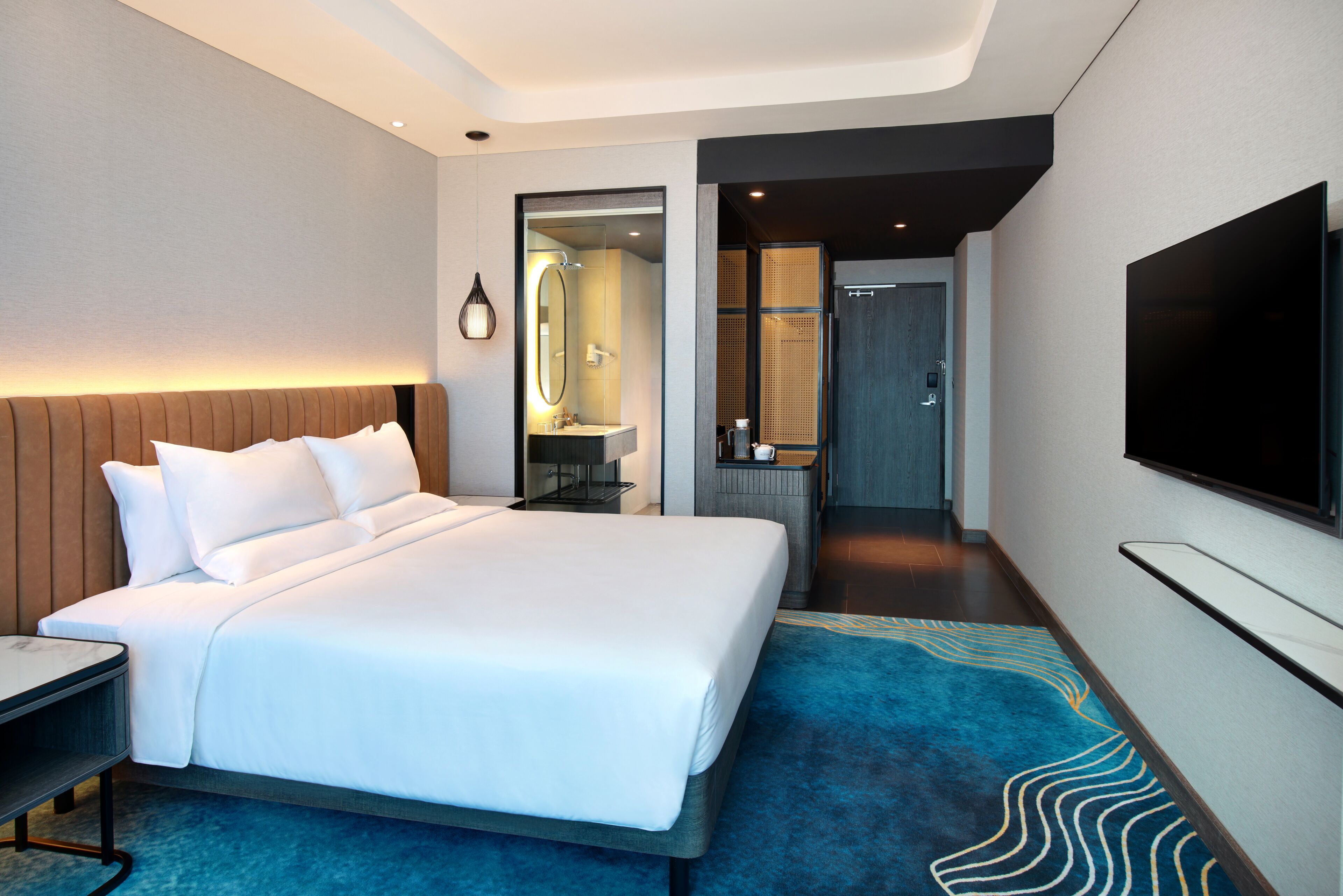 A modern hotel room with a large bed, a TV, a desk, and a bathroom visible through an open door.