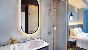 Casa de banho moderna com um espelho oval grande, lavatório branco e área de duche.