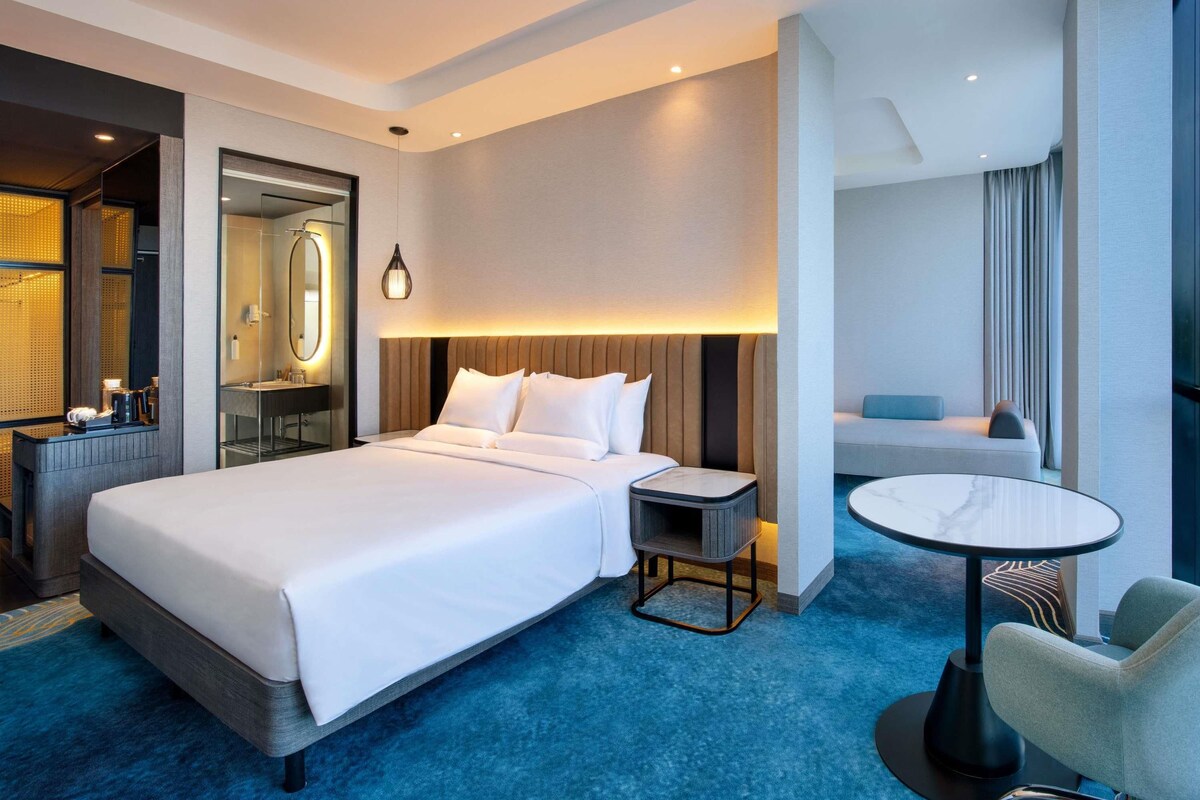 A modern hotel room with a large bed, bedside table, and a small round table.