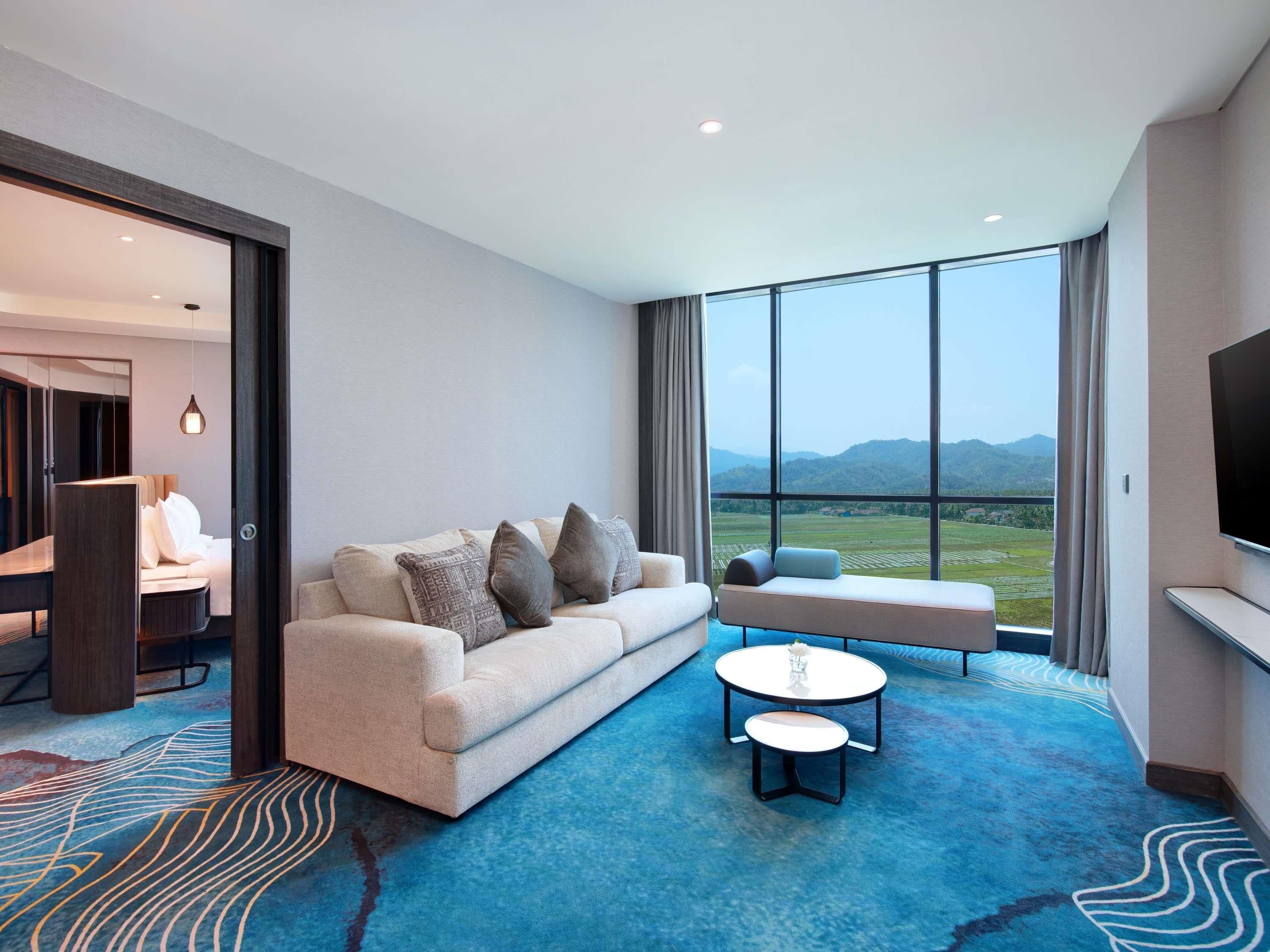 Une chambre d’hôtel moderne, dotée d’un canapé, d’une petite table et offrant une vue sur un paysage montagneux grâce à de grandes fenêtres.