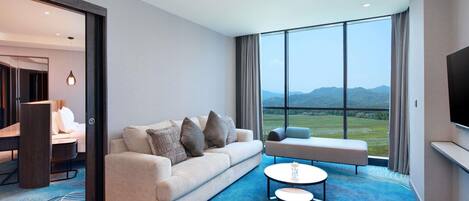 Une chambre d’hôtel moderne, dotée d’un canapé, d’une petite table et offrant une vue sur un paysage montagneux grâce à de grandes fenêtres.