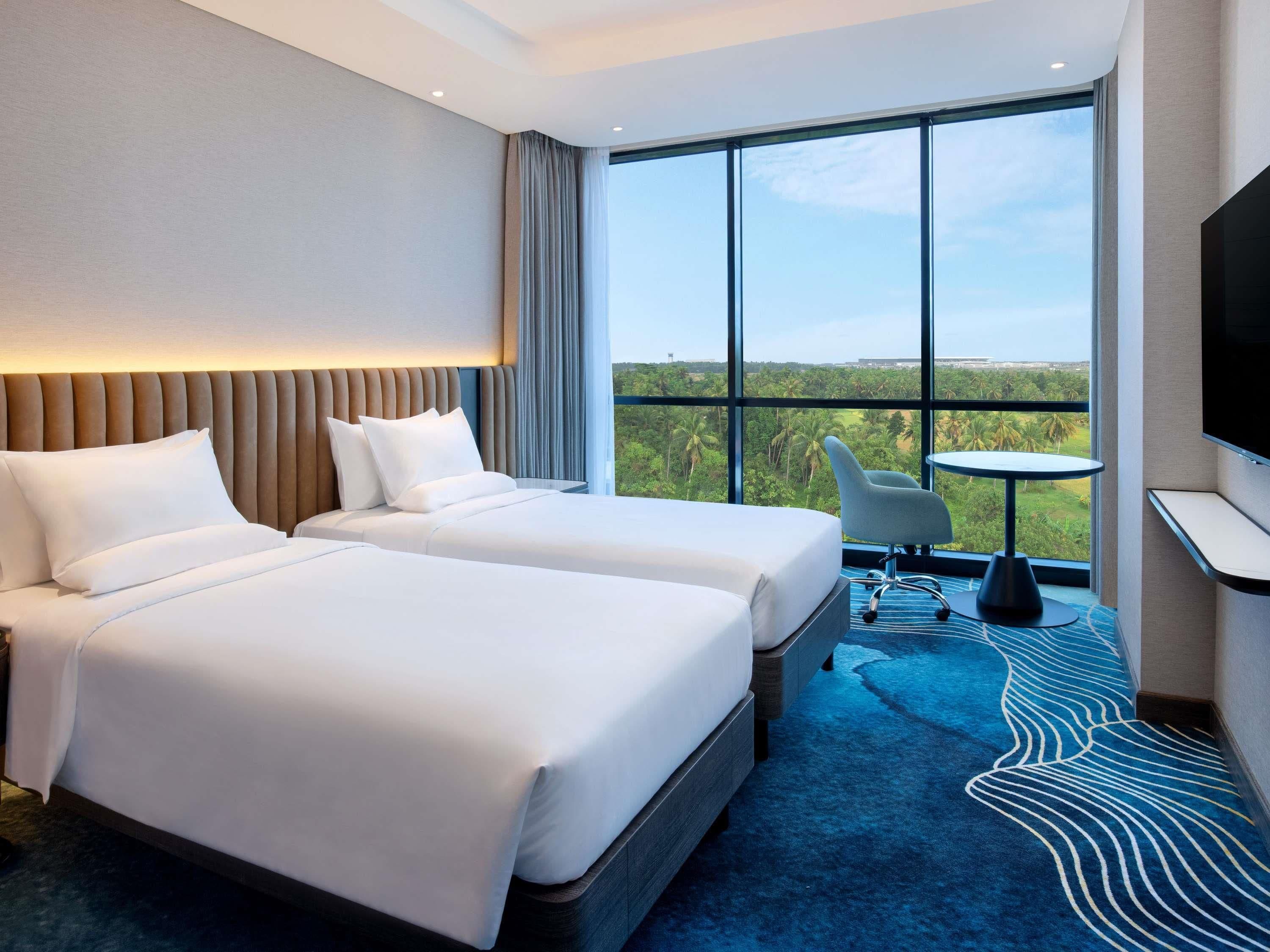 A hotel room with two beds, a large window with a view, a small table, and a TV.