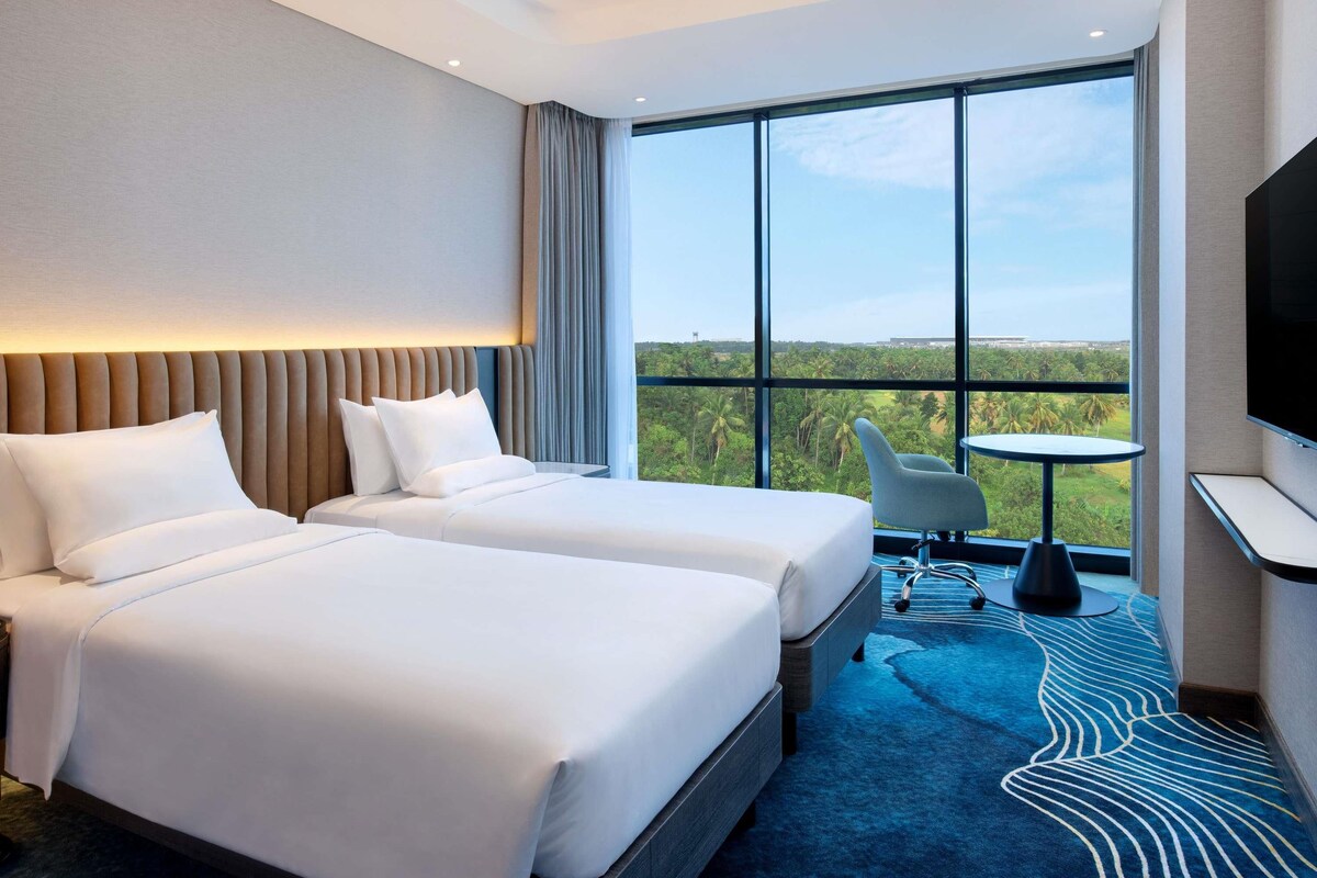 A hotel room with two beds, a large window with a view, a small table, and a TV.