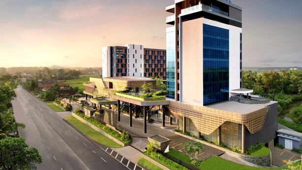 Um hotel moderno com um destaque para o letreiro 'NOVOTEL', apresentando um design arquitetônico único com uma combinação de vidro e tijolo, e um jardim no terraço.