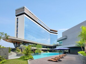 A modern hotel with a swimming pool, lounge chairs, and a well-maintained garden. - Novotel Yogyakarta International Airport Kulon Progo (Temon)