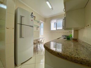 A kitchen with a white refrigerator, a glass shelf, a window with blinds, and a granite countertop.