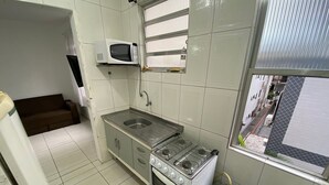 A compact kitchen with a gas stove, a microwave, a sink, and a gas cylinder. - Foot in the sand Beach corner of the fort (Praia Grande)