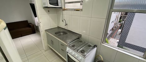 A compact kitchen with a gas stove, a microwave, a sink, and a gas cylinder.