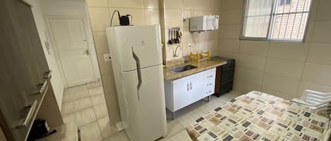 A compact kitchen with a refrigerator, microwave, sink, and a dining table with a patterned tablecloth.