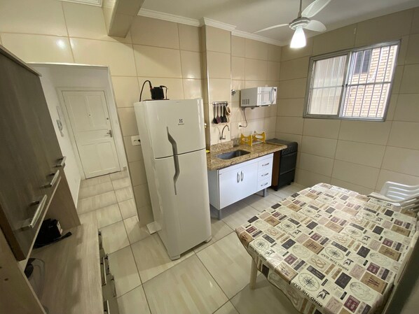 A compact kitchen with a refrigerator, microwave, sink, and a dining table with a patterned tablecloth.