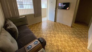 Ett vardagsrum med en brun soffa, en tv på väggen och mönstrade golvplattor.