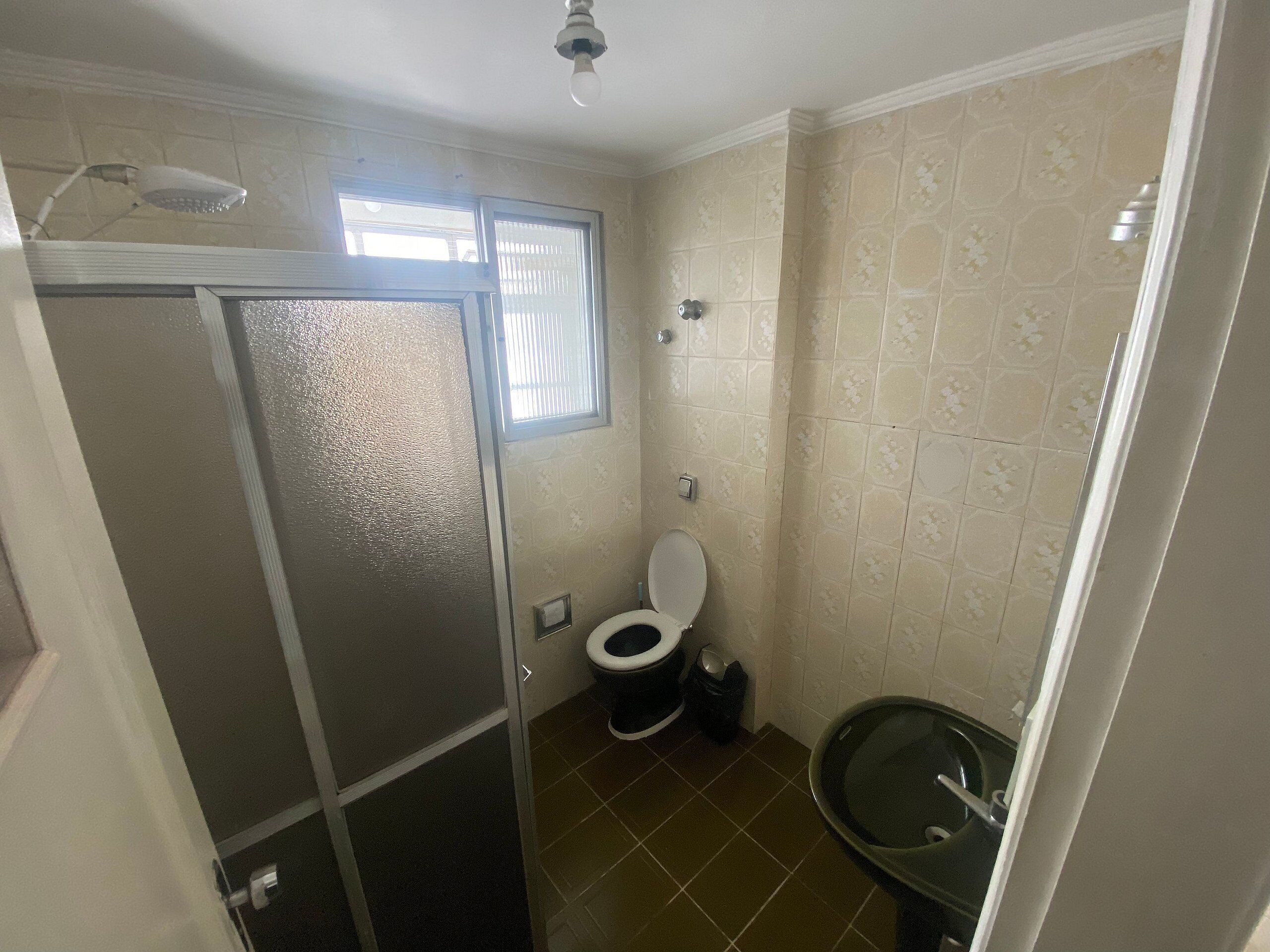 A compact bathroom with a toilet, a small sink, and a shower stall.