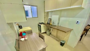 A compact kitchen with a dining area, a gas stove, a sink, and a window with blinds. - Foot in the sand Corner of Fort II - Tiradentes 3 (Praia Grande)
