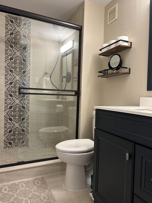 Et badeværelse med glasbrusekabine, toilet og vaskebord med spejl.
