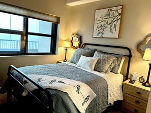 Un lit bien fait, recouvert d’une courtepointe matelassée, une lampe de chevet, une horloge et une œuvre d’art encadrée au mur.