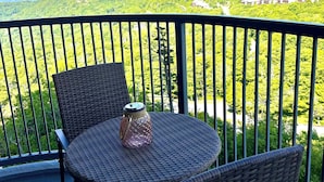 En balkon med fletmøbler, et glas og udsigt over et grønt landskab med bygninger i det fjerne.