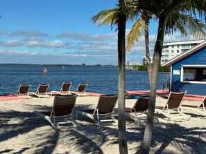 A beach with sun loungers, a palm tree, and a building labeled "ULTRA 1000" in the background. - Surf’s Up! Beachside home/ Riverfront Club access (Cocoa Beach)
