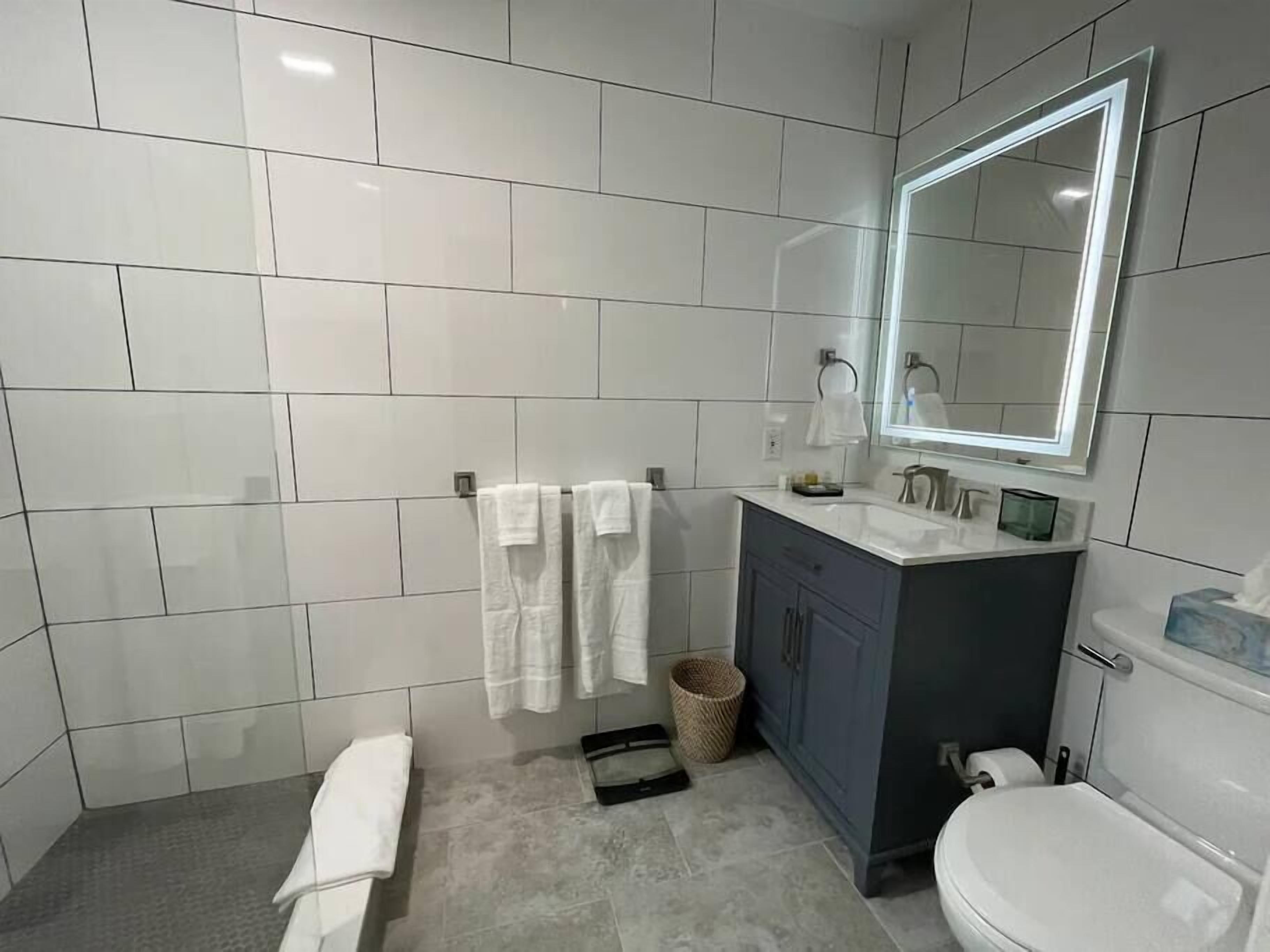 A modern bathroom with white tiles, a dark-toned vanity, a large mirror, and a toilet.