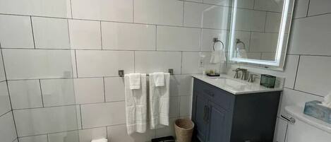 A modern bathroom with white tiles, a dark-toned vanity, a large mirror, and a toilet.