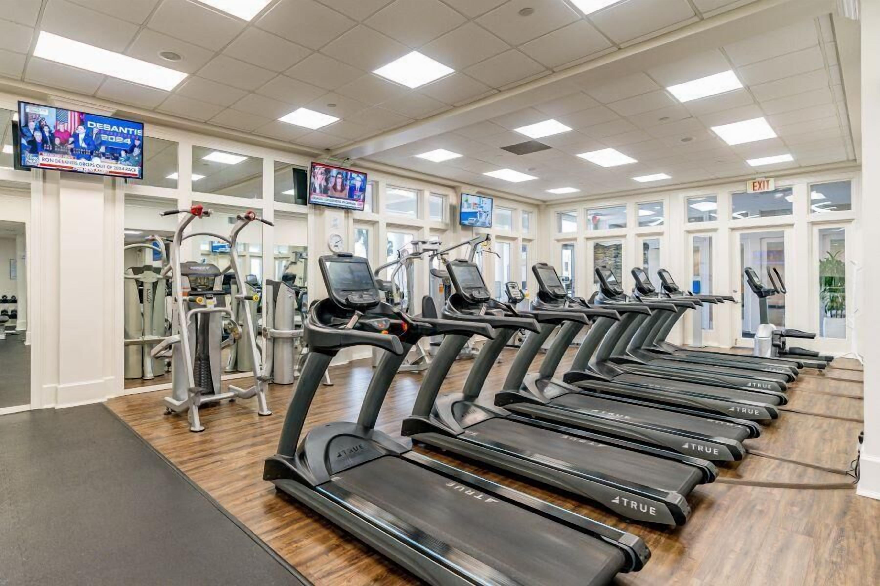 A gym with multiple treadmills, weight machines, and a television displaying an event.
