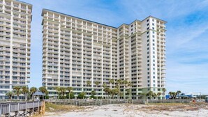 A high-rise hotel with multiple balconies, a beach view, and a wooden boardwalk.