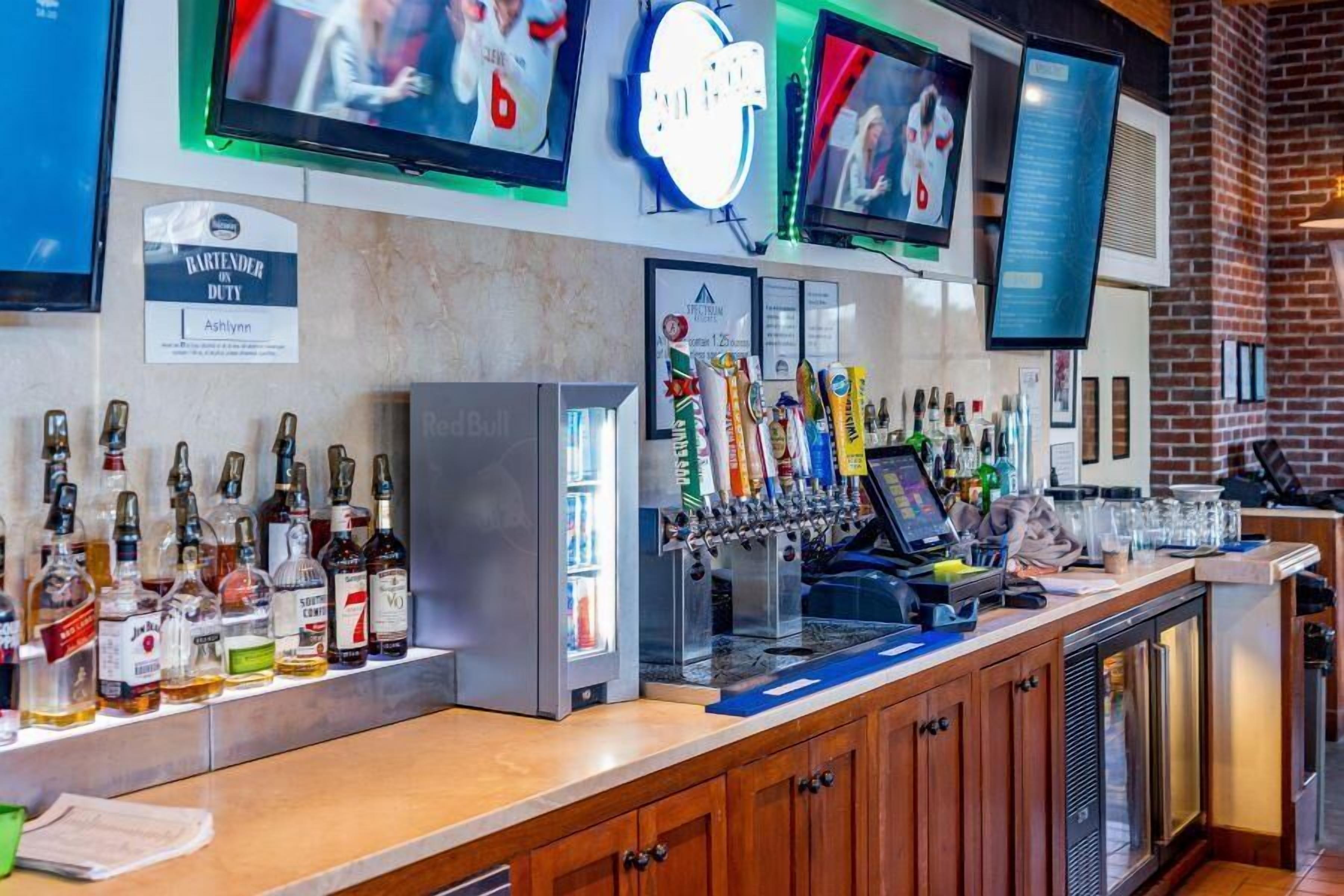 A bar area with a variety of liquor bottles, a tap system, and a digital menu display.