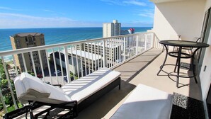Un balcon avec vue sur l’océan, une chaise longue, une petite table et une balustrade blanche.