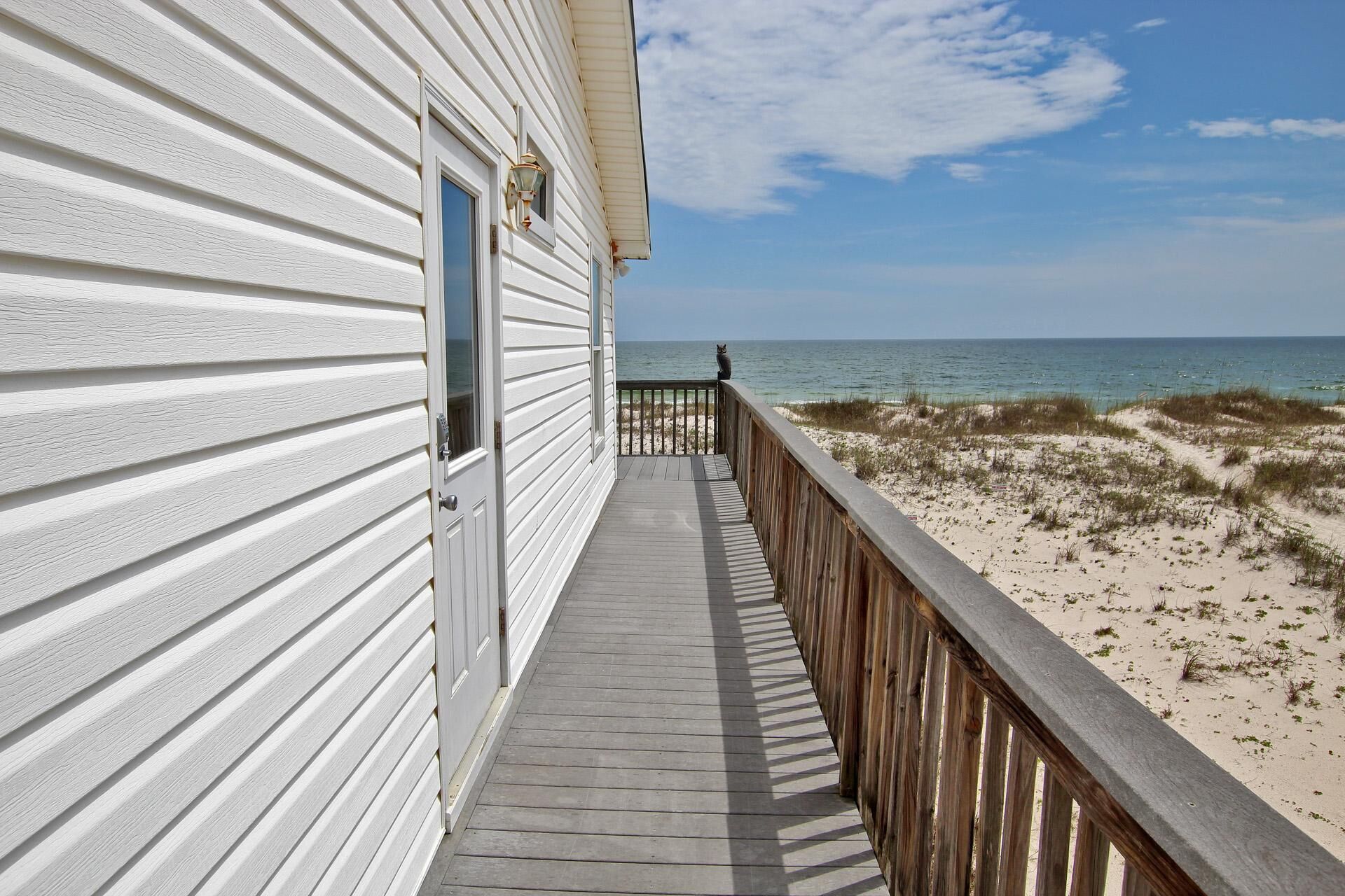 A wooden deck leading to a beach with a white building on the left.