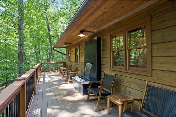 A wooden cabin with a deck, outdoor seating, and a fireplace.