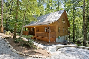 A wooden cabin with a porch, surrounded by trees.