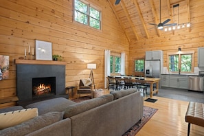A log cabin interior with a fireplace, seating area, dining table, and kitchen.