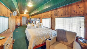 Ein Holzblockhaus-Innenraum mit einem großen Bett, einem Sessel und einem Ventilator.