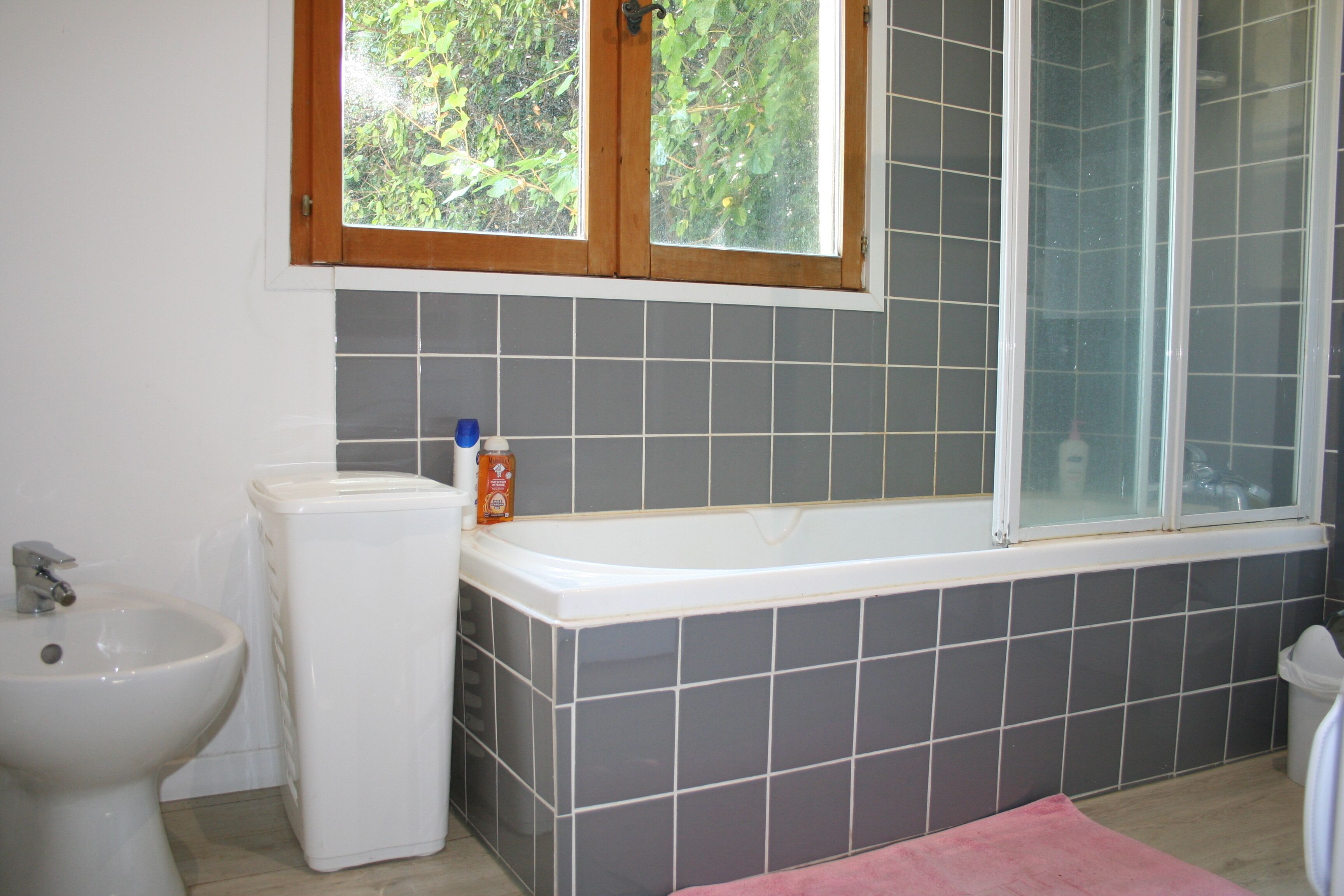 Ein Badezimmer mit Badewanne, Bidet und einem Fenster mit Blick ins Grüne.