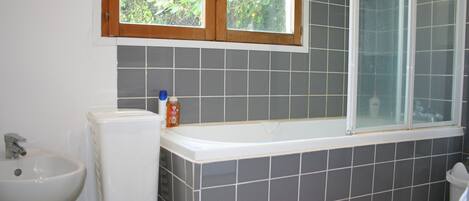 Ein Badezimmer mit Badewanne, Bidet und einem Fenster mit Blick ins Grüne.