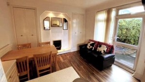 A living room with a wooden dining table, chairs, a black sofa with a patterned throw, and a fireplace. - Budgeted Shared Residence near Coventry Building Society (CBS) Ricoh Arena & M6 (Coventry)