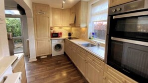 A kitchen with wooden cabinets, a washing machine, a microwave, and a double oven. - Budgeted Shared Residence near Coventry Building Society (CBS) Ricoh Arena & M6 (Coventry)