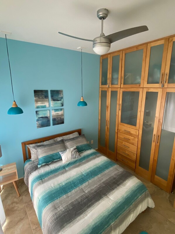 Un dormitorio con cama, armario de madera, ventilador de techo y dos lámparas colgantes.